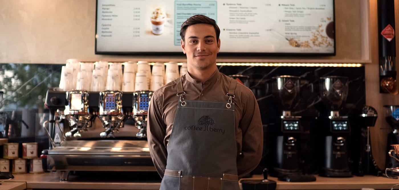 A smiling Coffee Berry barista in an apron behind the counter
