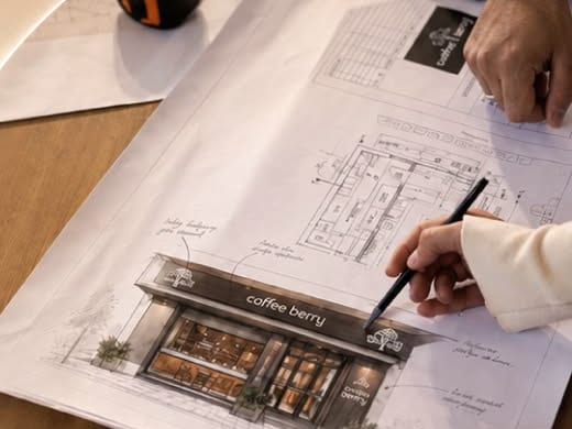 Αρχιτεκτονικά σχέδια και σκίτσο πρόσοψης καταστήματος Coffee Berry πάνω σε τραπέζι