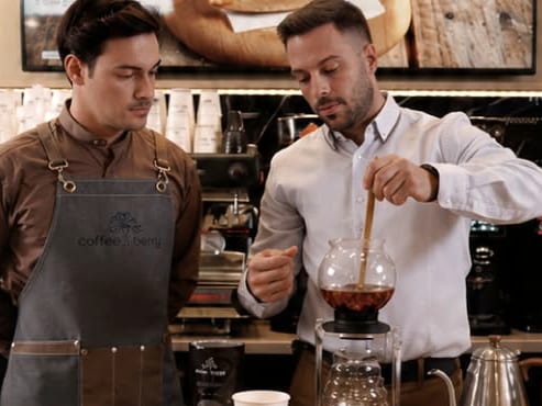 Barista και εκπαιδευτής της Coffee Berry ετοιμάζουν καφέ σε σιφόν στον πάγκο