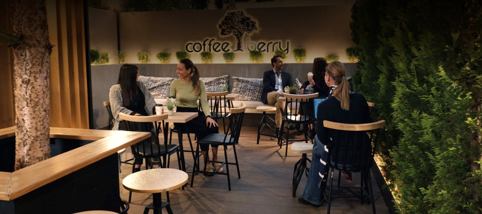 A Coffee Berry garden lounge at dusk, with the glowing tree logo and guests at the tables